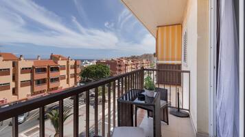 A balcony with a view of buildings, a table with chairs, and a potted plant.