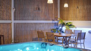 A hot tub area with wooden walls, a dining table with chairs, and hanging lights. - Porfyra Suite 1 (Agistri)