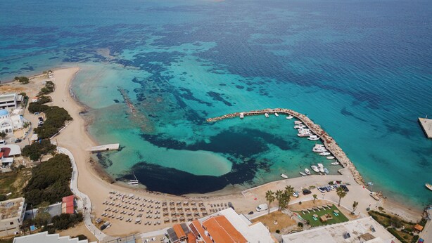An aerial view of a coastal area with a beach, marina, and buildings. - Porfyra Suite 1 (Agistri)