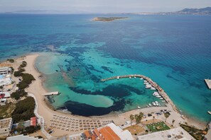 An aerial view of a coastal area with a beach, marina, and buildings. - Porfyra Suite 1 (Agistri)