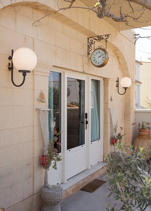 A building facade with a clock, two doors, and wall-mounted light fixtures. - Porfyra Suite 1 (Agistri)