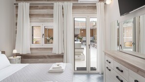 A modern hotel room with a bed, a vanity with a mirror, a flat-screen TV, and a sliding glass door leading to a balcony. - Porfyra Suite 1 (Agistri)