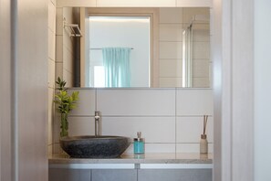 A bathroom with a stone sink, a mirror, and a plant. - Porfyra Suite 1 (Agistri)
