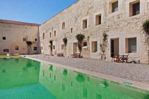 A courtyard with a swimming pool, stone buildings, and outdoor seating.