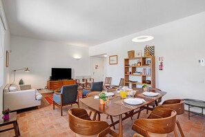 A dining area with a table set for four, surrounded by wooden chairs, a television, and a bookshelf.