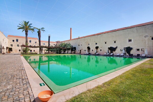 A swimming pool with lounge chairs, palm trees, and a building with a red roof.