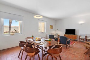 A spacious living area with a dining table, chairs, a sofa, a TV, and a balcony view.