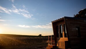 Una cabaña de madera moderna con una escalera que lleva a la entrada, ubicada en un campo bajo un cielo despejado.