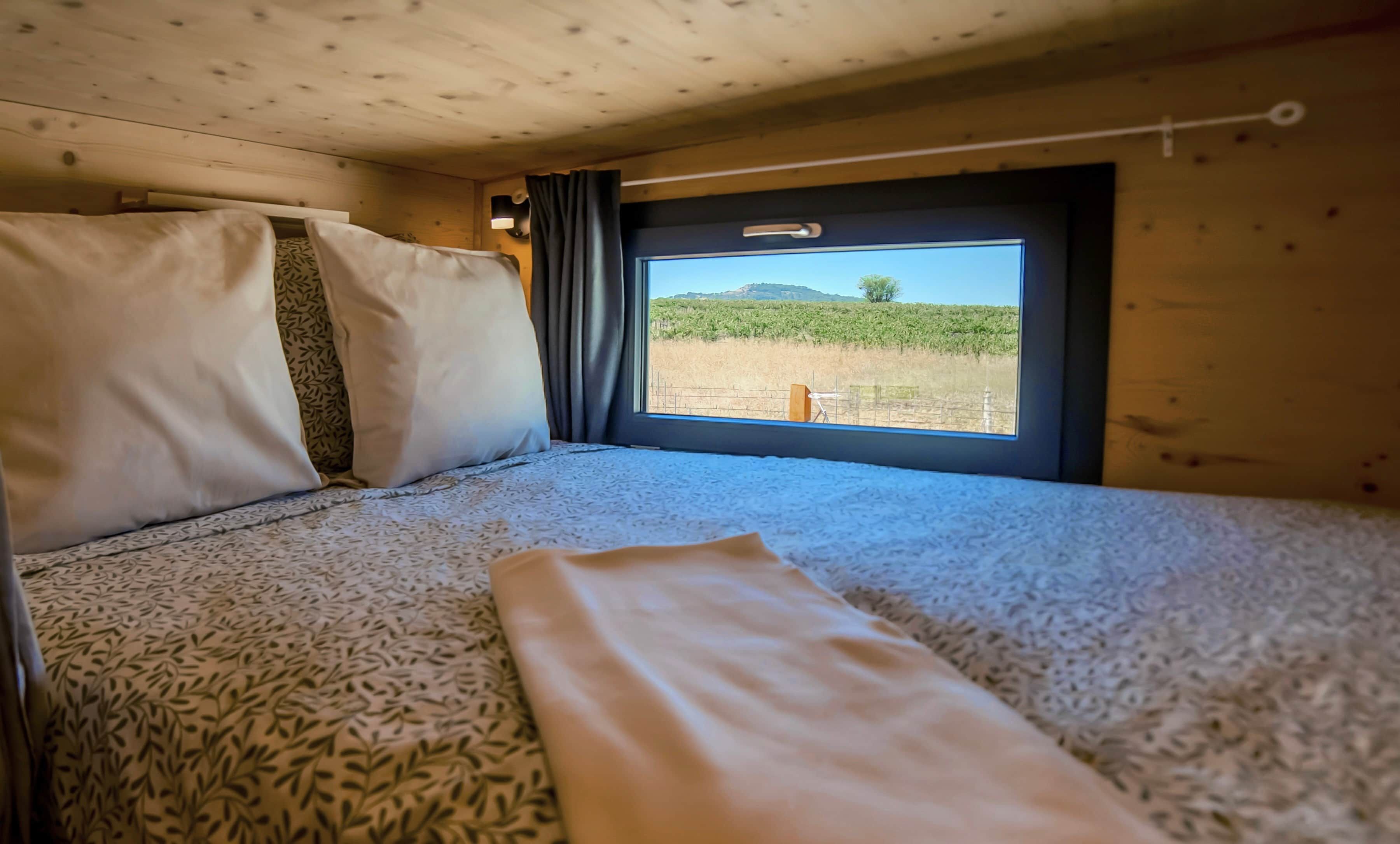 A bed with patterned bedding and a window with a view of a field and hills.