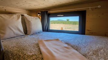 A bed with patterned bedding and a window with a view of a field and hills.