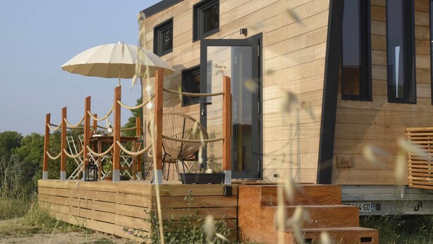 Un edificio moderno de madera con terraza de madera, una silla de mimbre y un paraguas blanco.