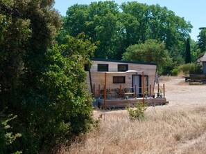 A small wooden cabin with a deck, surrounded by trees and dry grass.