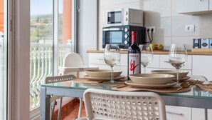 A dining area with a glass table, white chairs, and a view of the city through a balcony.