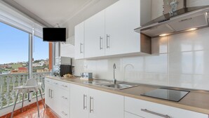 A modern kitchen with white cabinets, a stainless steel sink, and a flat-screen TV mounted above the counter.