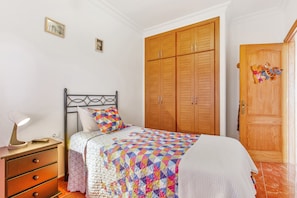A bedroom with a bed, wooden wardrobe, and a nightstand with a lamp.