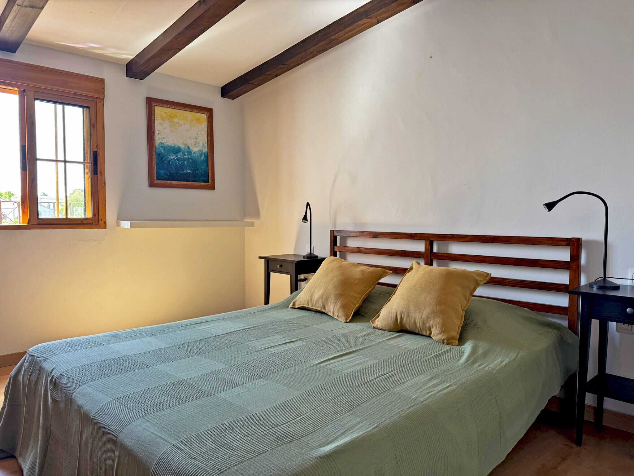A bedroom with a bed, two bedside tables, a nightstand, a lamp, and a window.