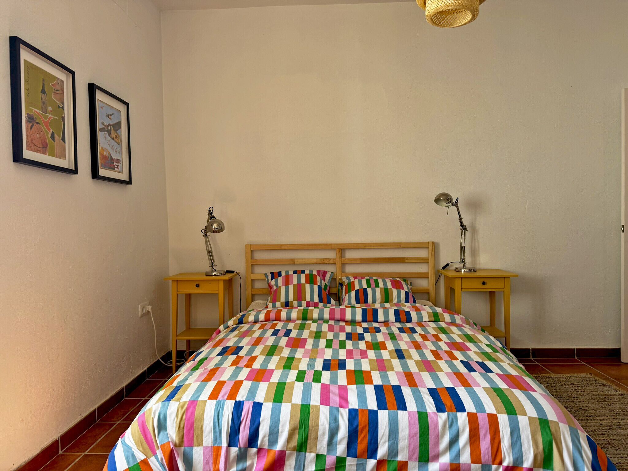 Une chambre à coucher avec un lit en bois, deux tables de chevet, deux lampes et une couvre-lit rayée aux couleurs vives.