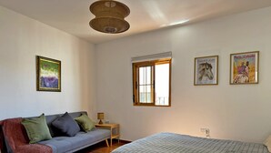 Un dormitorio con cama, sofá, ventana y dos cuadros en la pared.