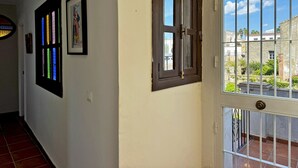 Un pasillo con pared blanca, una puerta con ventanal y un balcón con barandilla metálica.