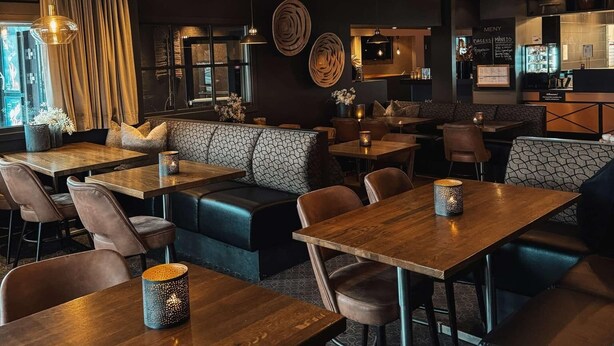 Un restaurante con mesas y puestos de madera, iluminación colgante y una pizarra de menú.