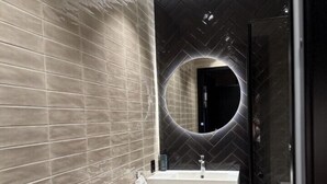 Un baño moderno con pared de azulejos grises, un lavamanos blanco y una pared negra con motivo de espiga detrás del espejo.