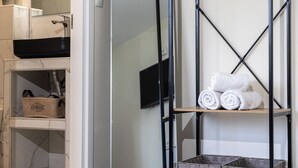 A bathroom with a black sink, a mirror, a towel rack with rolled towels, and a storage basket. - Nobia 8 (Athens)