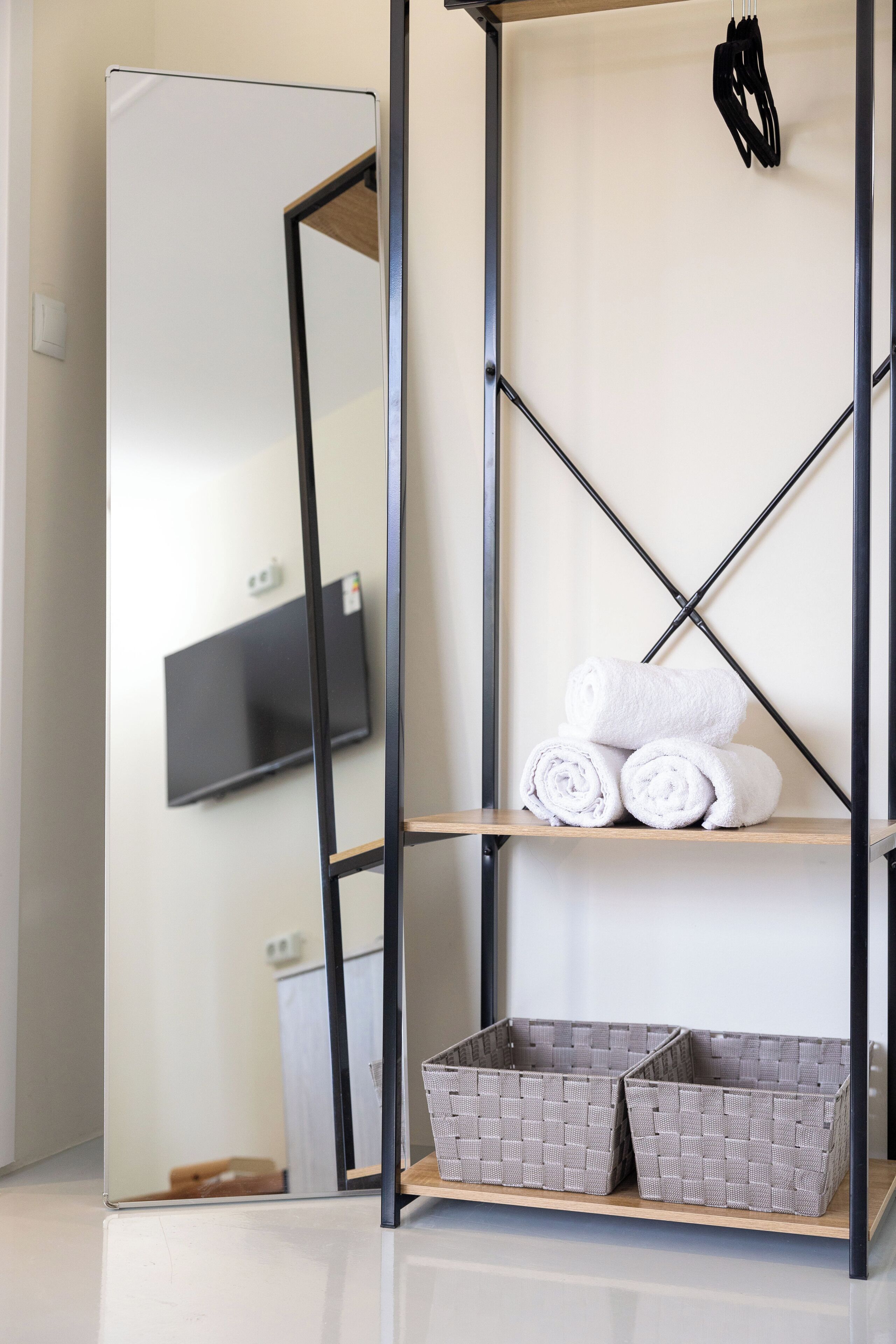 A modern bathroom with a mirror, a shelf with rolled towels, and two wicker baskets.