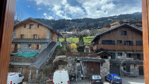 A rural village with wooden houses, a stone building, and a parking area with cars and a van. - Apartment: Chez Pierre (Courchevel)