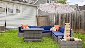 A backyard with a sectional sofa, a table, and a wooden Jenga tower. - Retro Indy stay-sleeps 10! Big backyard, outdoor games, BBQ, 5 min from Downtown (Indianapolis)