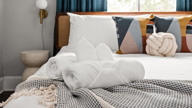 A neatly made bed with white towels, a patterned throw blanket, and a geometric pillow. - Retro Indy stay-sleeps 10! Big backyard, outdoor games, BBQ, 5 min from Downtown (Indianapolis)