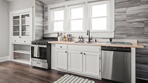 A kitchen with white cabinetry, a stainless steel dishwasher, a gas stove, and a window above the sink. - Retro Indy stay-sleeps 10! Big backyard, outdoor games, BBQ, 5 min from Downtown (Indianapolis)