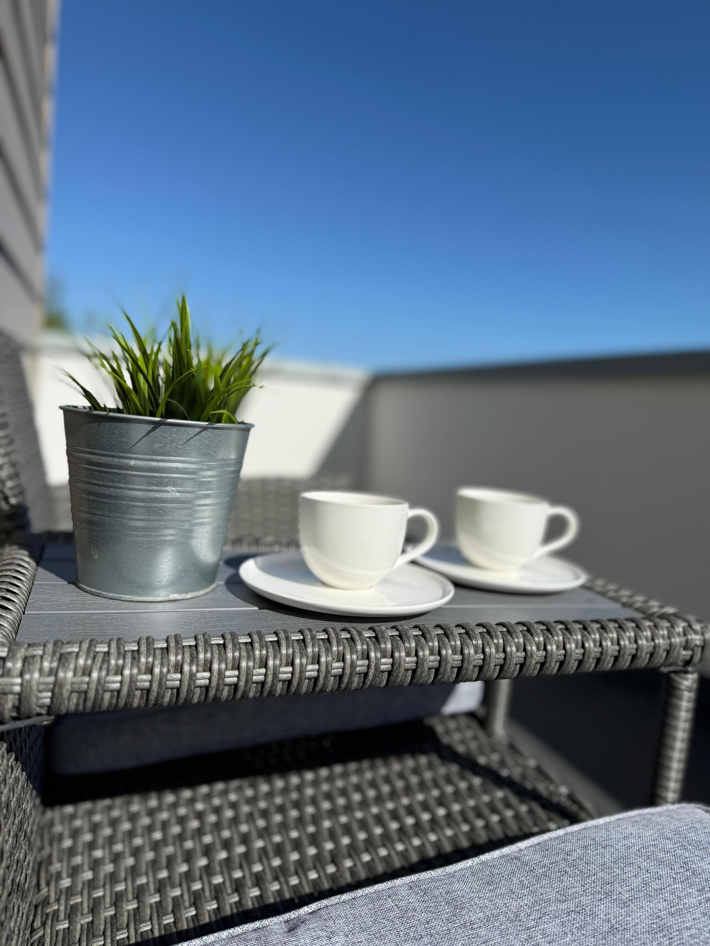 A wicker outdoor seating area with a metal pot and two white cups on a table.