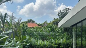A pool with two wooden lounge chairs on a wooden deck, surrounded by lush greenery and a modern building in the background. - Nova by OXO (Canggu)