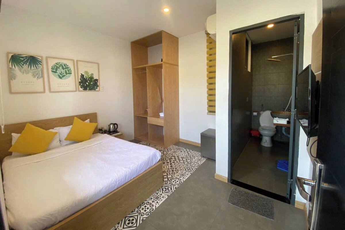 Una habitación de hotel con cama, armario de madera, baño con inodoro y lavabo, y televisor.
