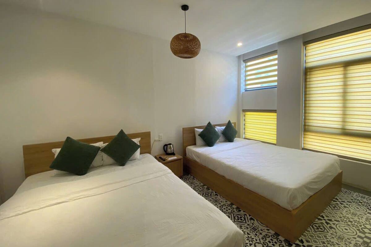 Habitación de hotel con dos camas, una mesita de noche, una cafetera y una lámpara colgante.