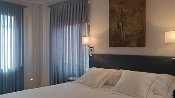 A hotel room with a large bed, two bedside lamps, a painting on the wall, and sheer curtains.