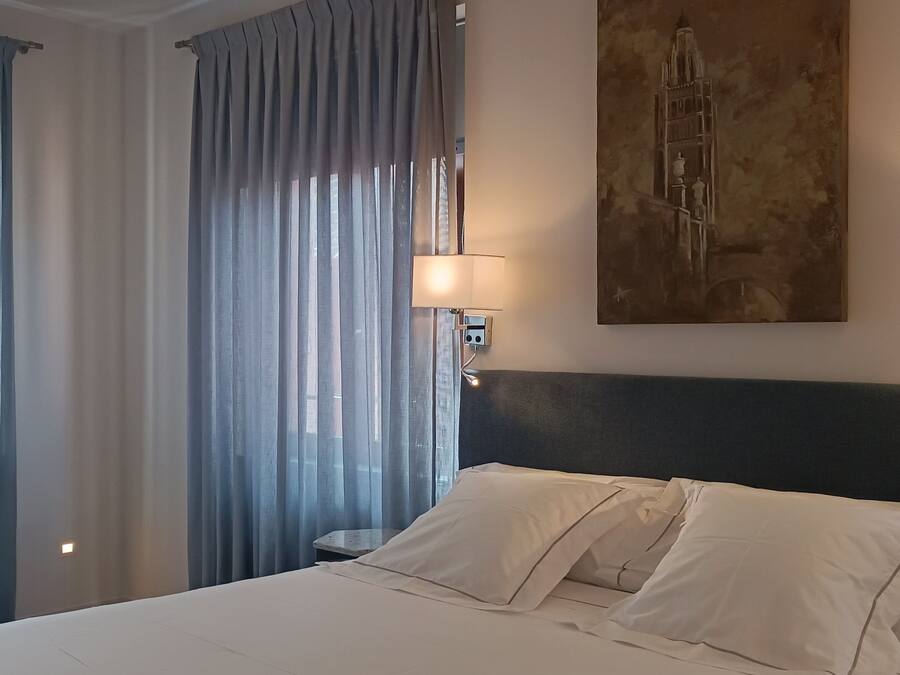 A hotel room with a large bed, two bedside lamps, a painting on the wall, and sheer curtains.