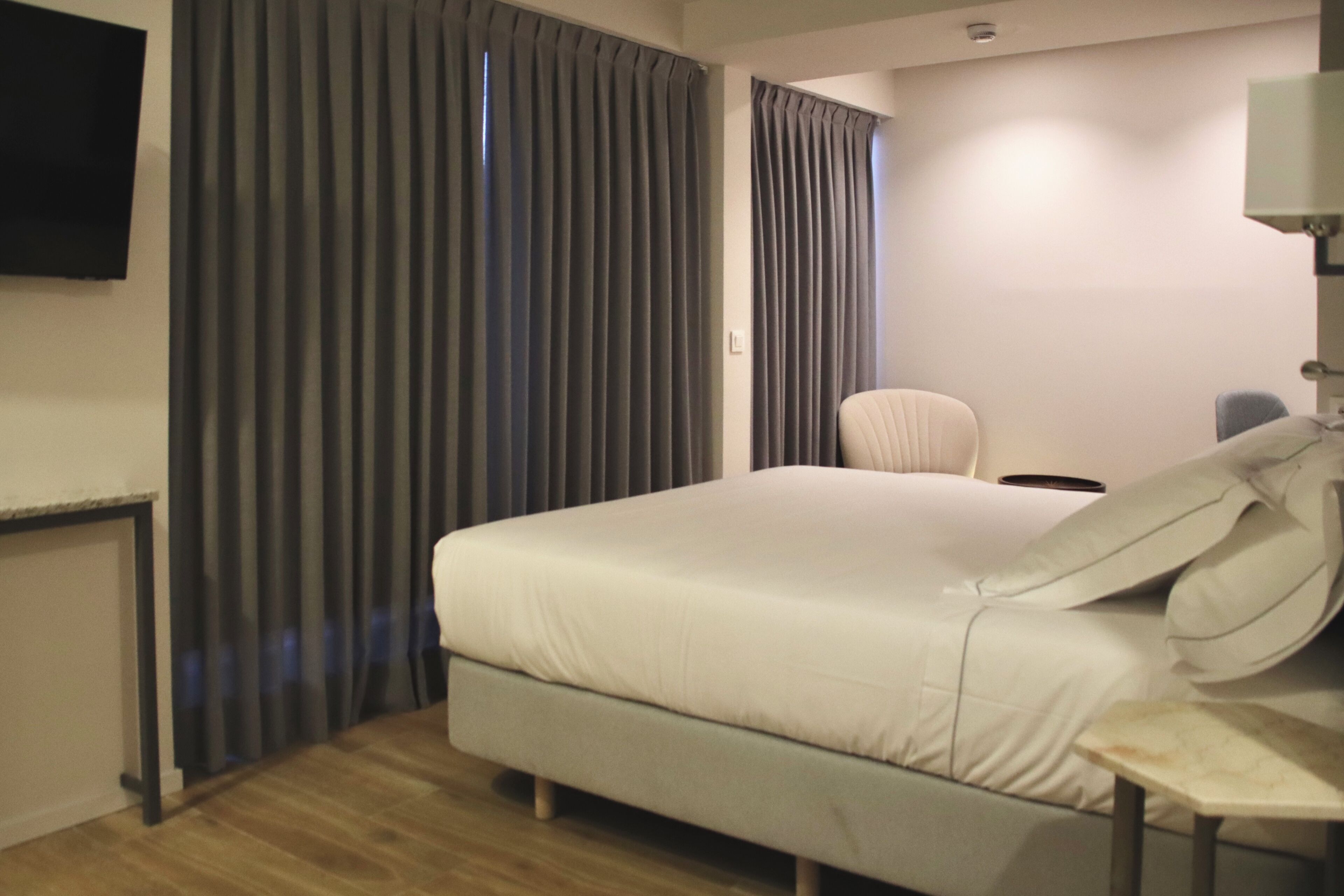 Una habitación de hotel con una cama, una silla, un escritorio y un televisor montado en la pared.
