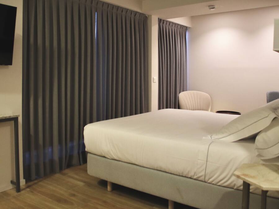 A hotel room with a bed, a chair, a desk, and a TV mounted on the wall.