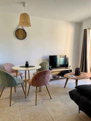 Una sala de estar moderna con una mesa redonda, dos sillas, un sofá, un televisor y una lámpara colgante.