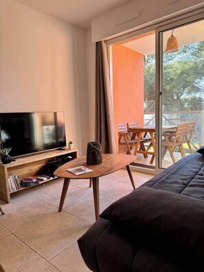 Una sala de estar moderna con una televisión de pantalla plana, una mesita de madera, un sofá y un balcón con mesa y sillas.