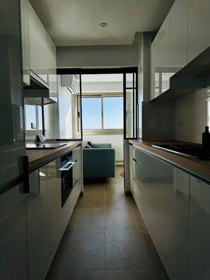 Cozinha estreita com eletrodomésticos modernos, um sofá azul-turquesa e uma grande janela com vista.