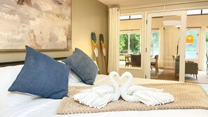 Quarto de hotel com cama, duas almofadas, arranjo de toalhas, um quadro e vista para o exterior.