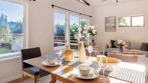 Uma sala de jantar com uma mesa posta para dois, um vaso com flores e vista para o exterior.
