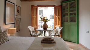 A bedroom with a bed, a bedside table with a lamp, two wicker chairs, a small round table with a vase of flowers, and a green wardrobe. - Castelar Suite, Villajoyosa Old Town, Seaview (La Vila Joiosa)