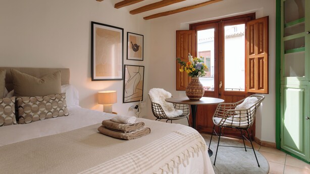 A bedroom with a bed, two chairs, a table, and a green door. - Castelar Suite, Villajoyosa Old Town, Seaview (La Vila Joiosa)