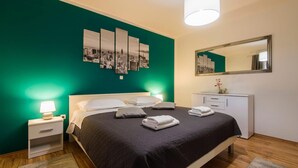 Ein Hotelzimmer mit Bett, Nachttischen, einem Schminktisch und einem Stadtbild an der Wand.
