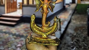Een hand houdt een gouden anker met ingewikkelde versieringen vast, voor een gebouw in de nacht.