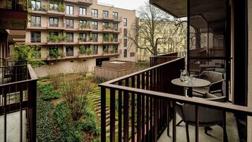 Ein Balkon mit Tisch und Stühlen, umgeben von viel Grün und Blick auf ein mehrstöckiges Gebäude mit Balkonen.