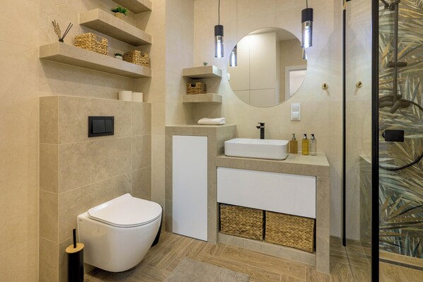 Une salle de bain moderne équipée de toilettes, d’un lavabo, d’un miroir et d’étagères contenant des articles de toilette.